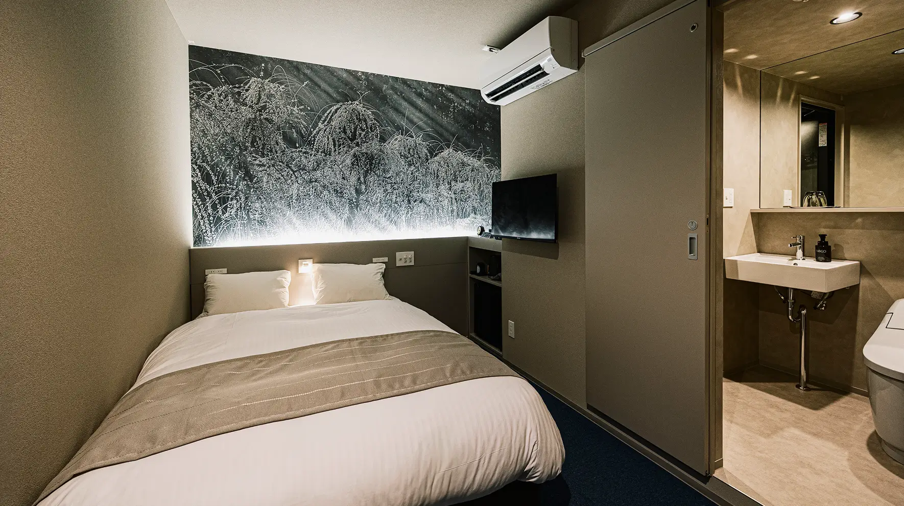 Compact room with a bed, toilet, and sink.